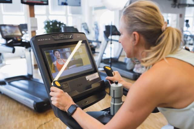 Blonde Frau beim Cardio Training in der Therme Wien Fitness. Beide Haende sind auf den Griffen.