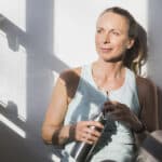 Frau atmet durch in der Pause beim Fitnesstraining und trinkt aus der Trinkflasche