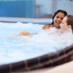 Zwei junge Frauen liegen entspannt im Whirlpool der Therme Wien.